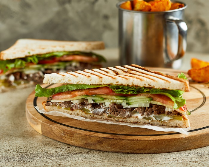 Grilled sandwich with meat and vegetables, served with potato wedges