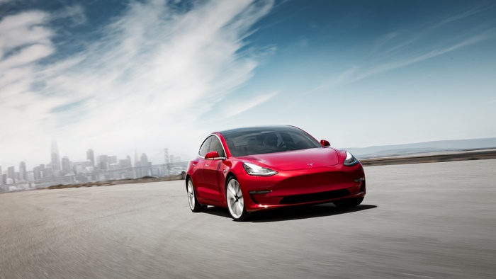 Red Tesla Model 3 driving with city skyline in background