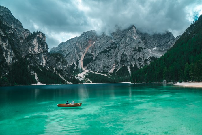 Two people in a canoe on a turquoise lake with mountains