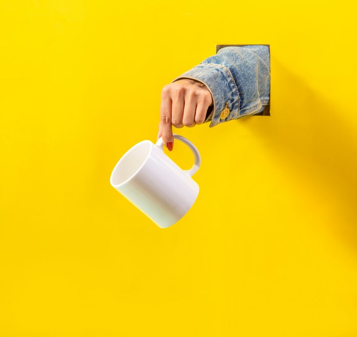 Hand holding a white mug through a yellow wall