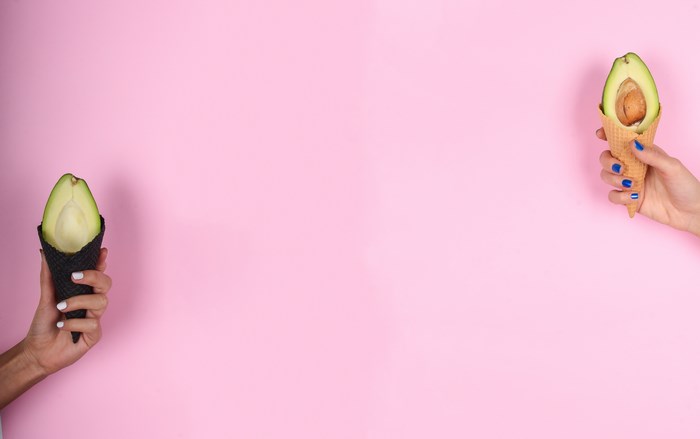 Hands holding avocado ice cream cones on pink background