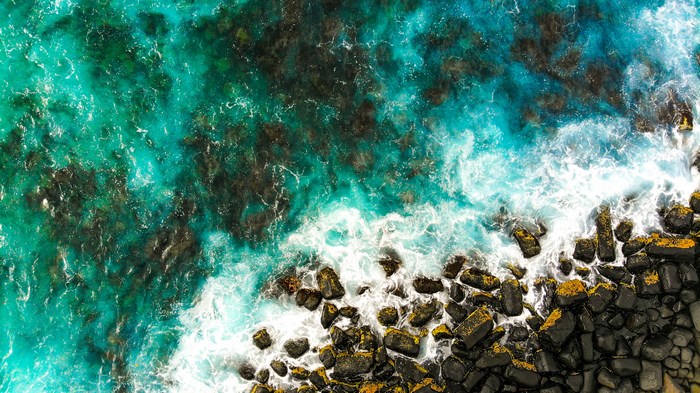 Aerial view of turquoise ocean waves crashing on a rocky coastline