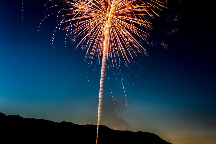 Fireworks exploding over a silhouetted mountain range at dusk