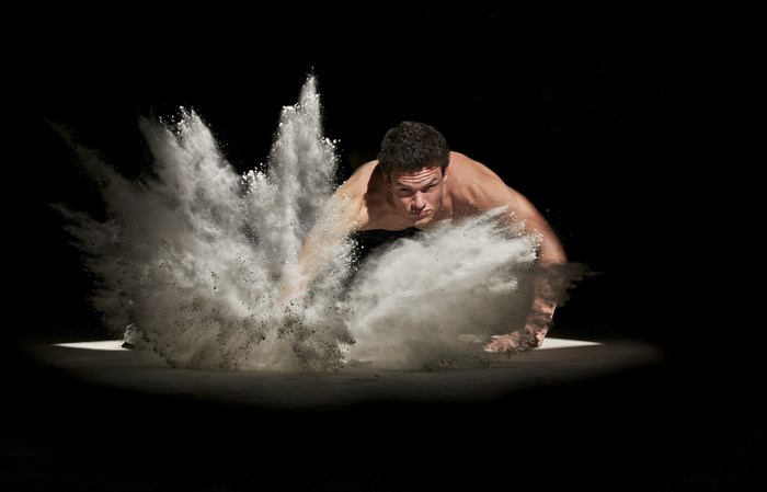 Muscular man doing push-ups in white powder explosion