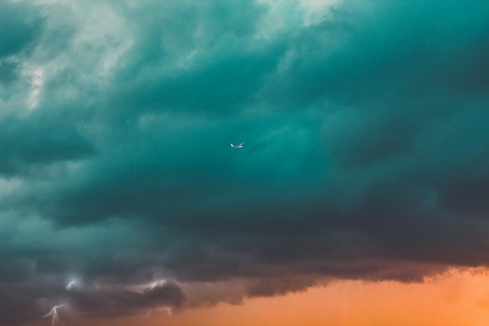 Airplane flying through stormy teal and orange sky with lightning