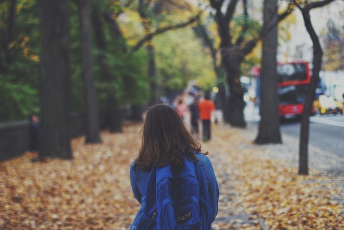Girl with backpack walking on autumn sidewalk
