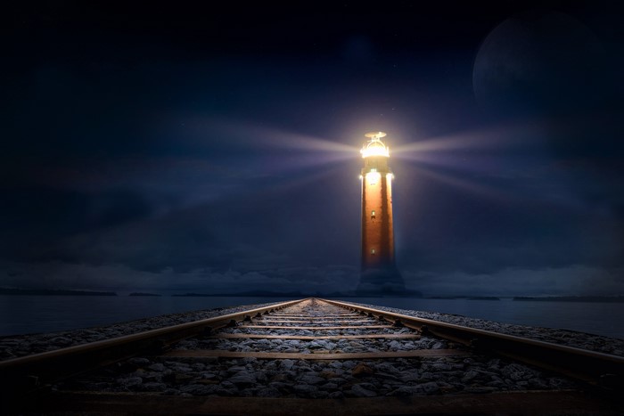 Railroad tracks leading to a lighthouse at night