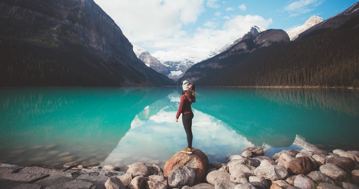 Woman standing on rock in front of turquoise lake and mountains