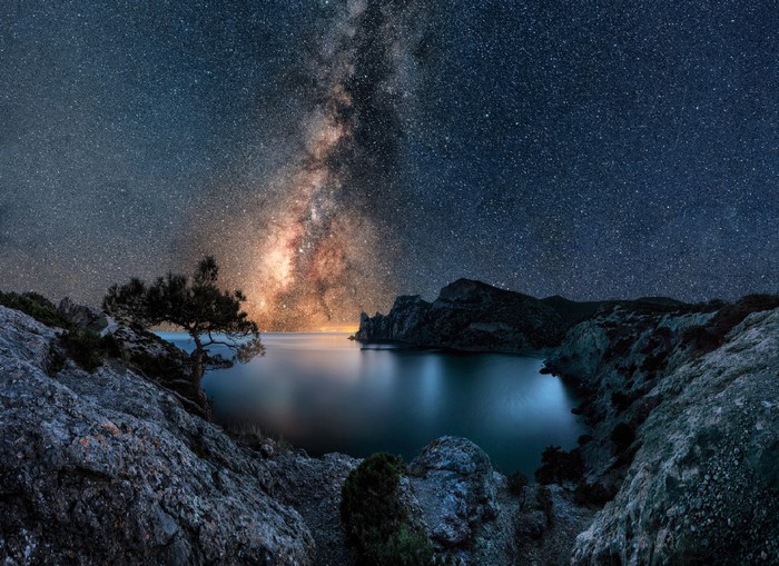 Milky Way over a calm bay with rocky shores