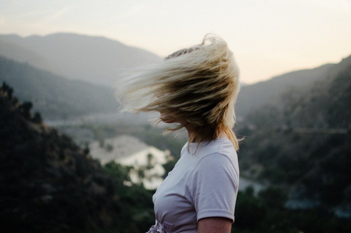 Woman with blonde hair blowing in the wind overlooking mountains