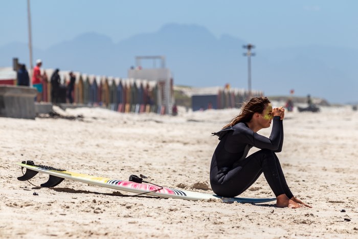 Woman in wetsuit with surfboard on sandy beach