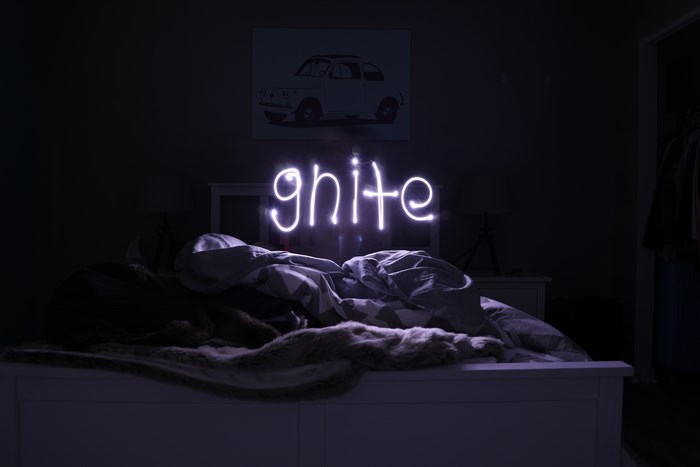 Light writing spelling 'gnite' above a messy bed