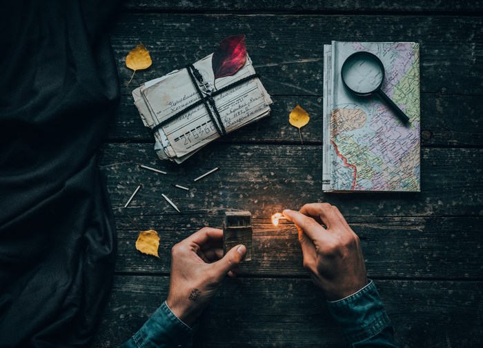 Hands lighting a match over a stack of letters and a map