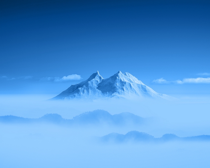 Snow-capped mountains above clouds under a blue sky
