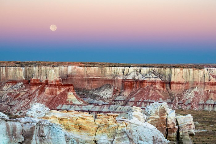 Moon over colorful desert canyon at dawn
