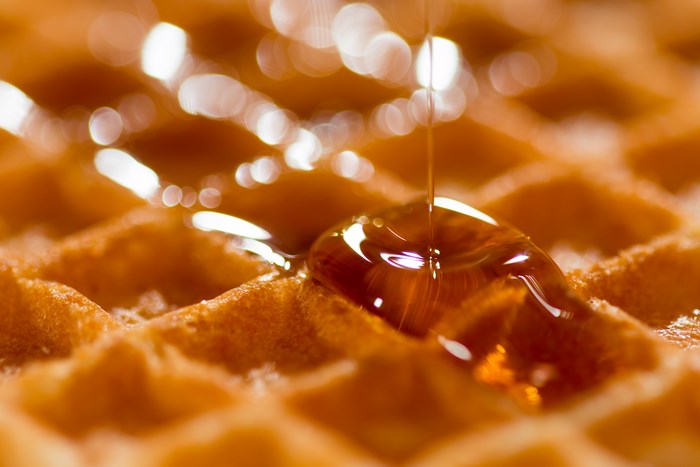 Syrup pouring on a golden waffle, macro shot