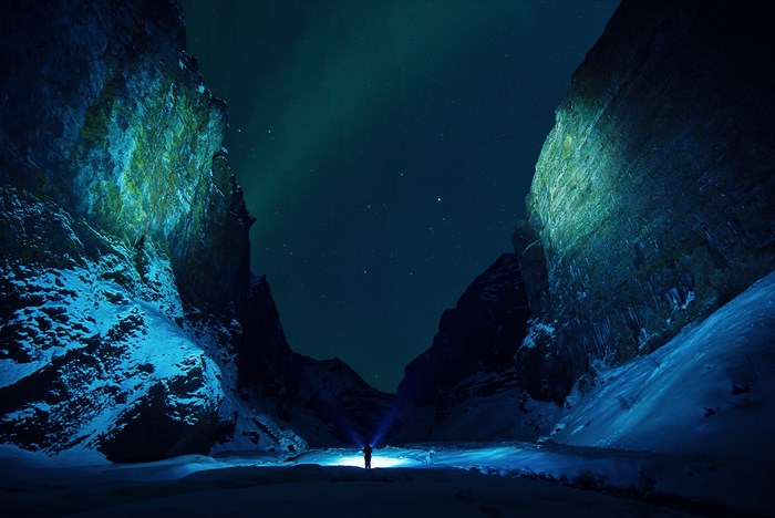 Person with flashlight in snowy canyon under Northern Lights
