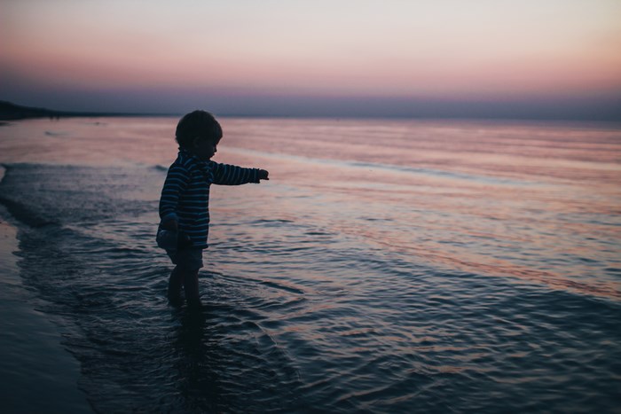 Child playing at the shoreline during sunset