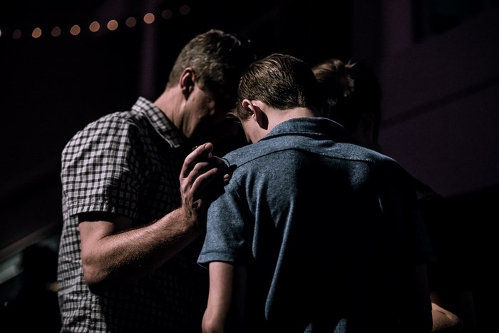 Man places hand on shoulder of young man while praying