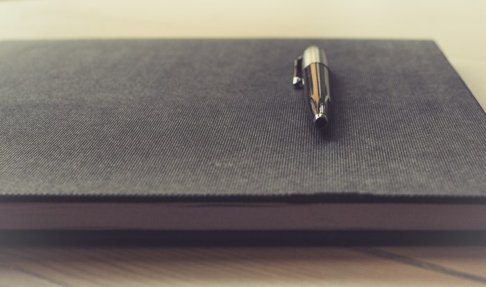 A silver pen rests on a dark gray notebook.