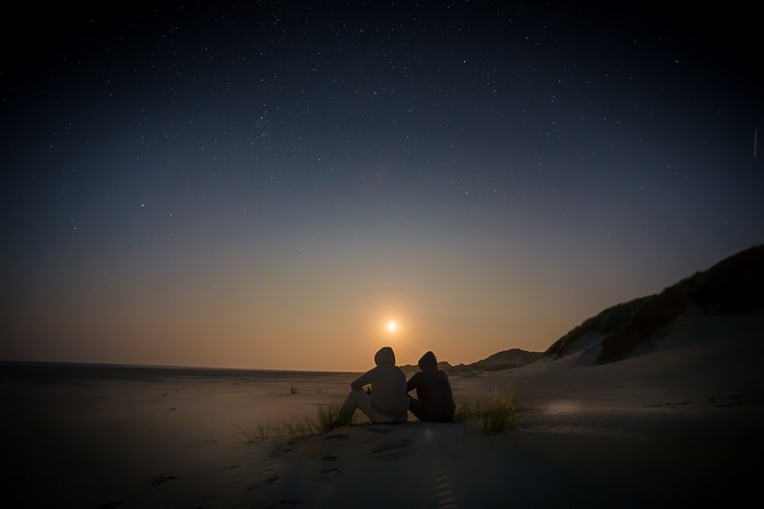 Two people watching the moonrise over a sandy beach