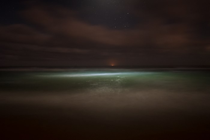Night ocean with glowing waves and distant light
