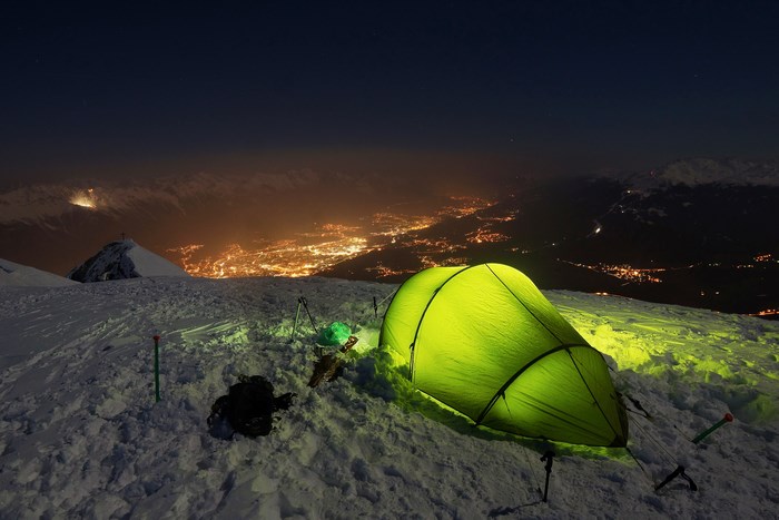 Green tent on snowy mountain overlooking Innsbruck at night