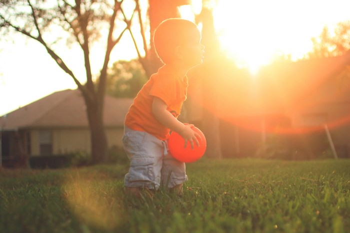 Boy holding an orange ball at sunset