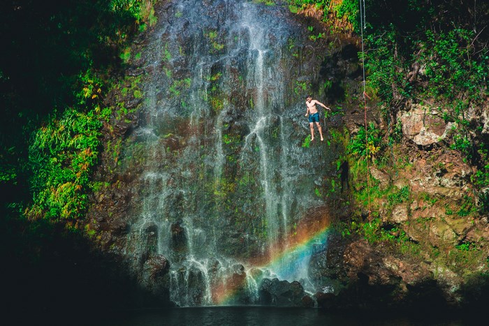 Man jumping off a waterfall with a rainbow