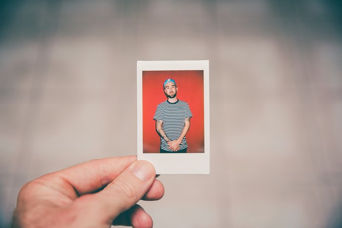 Man in striped shirt and baseball cap holding a polaroid