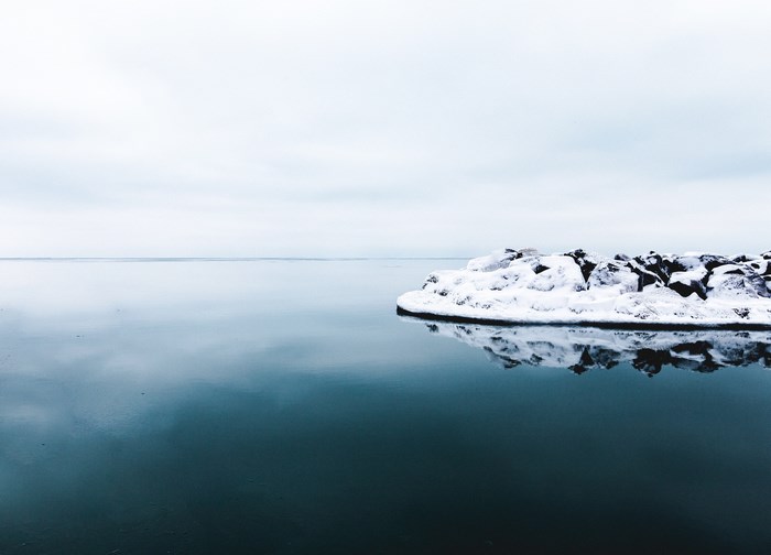 Snow-covered rocks in calm dark blue water