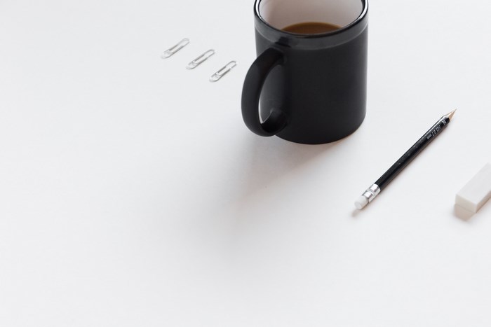 Black mug with coffee, pencil, eraser, and paperclips on white desk