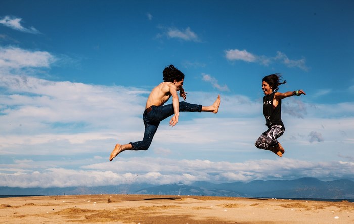 Two people jumping on a beach under a blue sky
