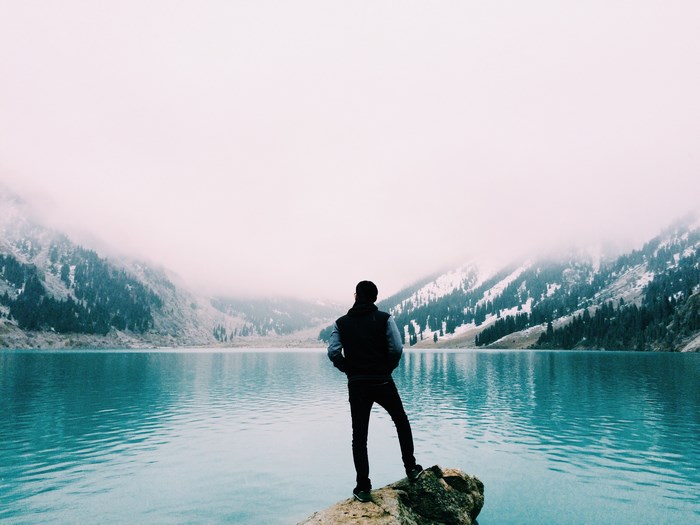 Man standing on rock overlooking turquoise lake and snowy mountains