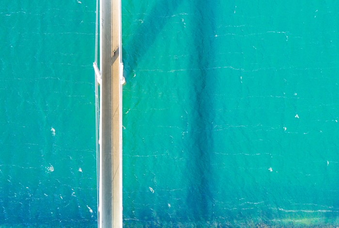 Aerial view of a bridge over turquoise water with a cyclist