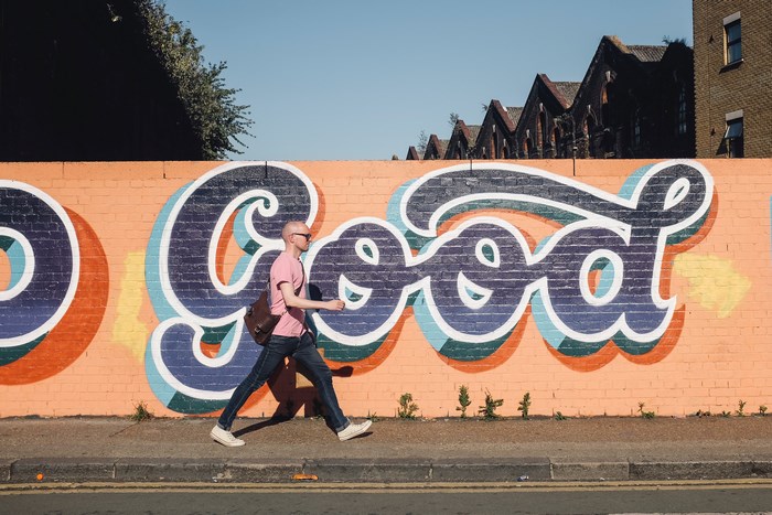 Man walks past graffiti art on a brick wall