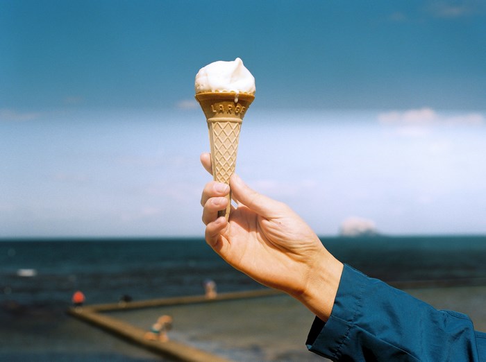 Hand holding a large ice cream cone by the sea