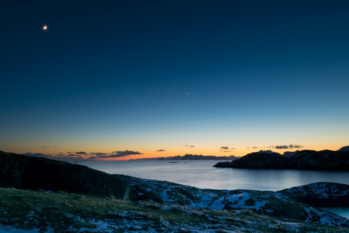 Moon and star over snowy mountains at dusk