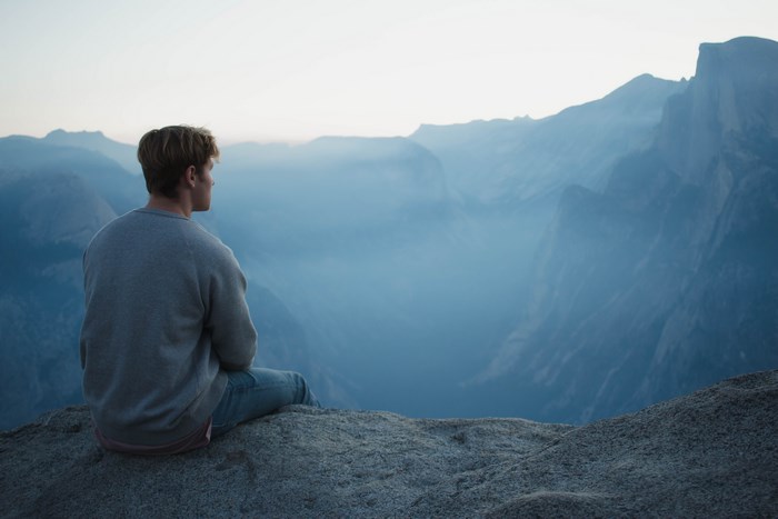 Man sitting on a rock overlooking a misty valley