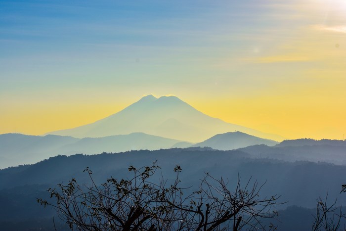 Mountain range silhouette at sunrise with yellow and blue sky