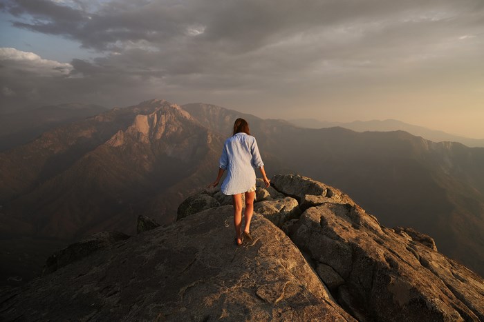 Woman walking on a rocky mountain summit at sunset