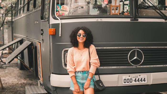 Woman in peach sweater and denim shorts in front of Mercedes bus