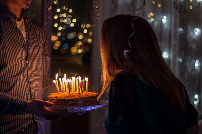 Man holds birthday cake with lit candles for woman