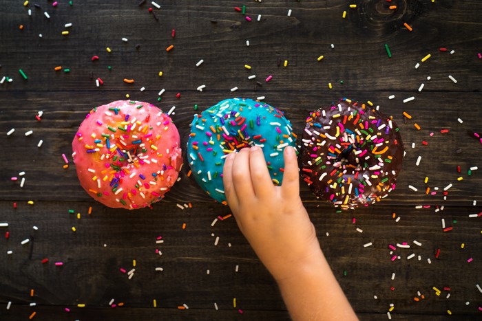 Child's hand reaching for colorful donuts with sprinkles