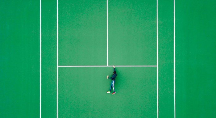 Person playing tennis on a green court from above