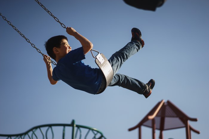 Asian boy swinging high on a playground swing