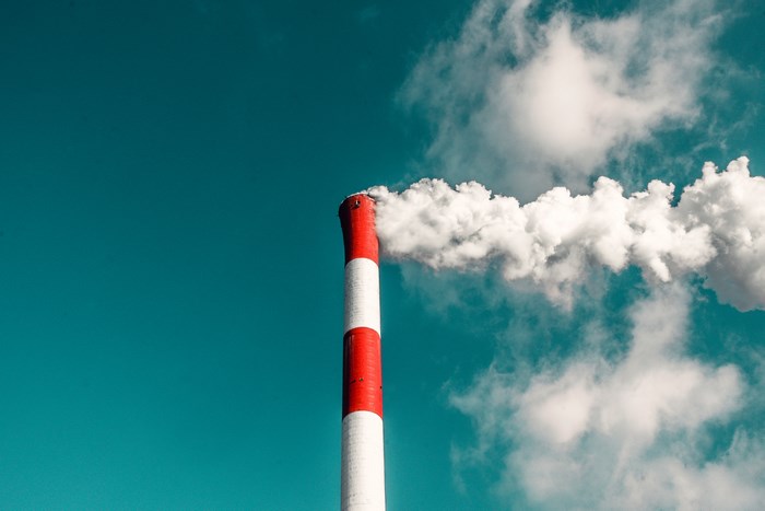 Red and white chimney emitting smoke against a teal sky