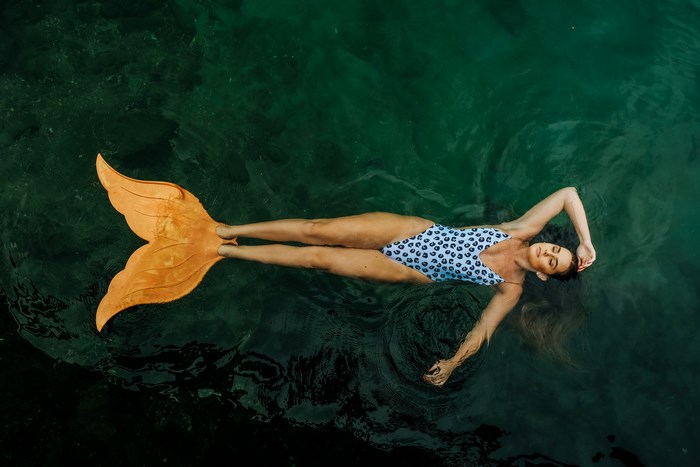 Woman in mermaid tail floating in dark water