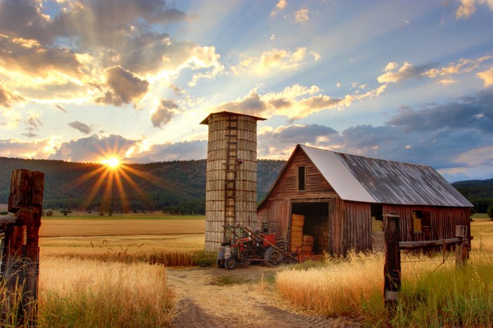 Sunset over a farm with barn, silo, and tractor