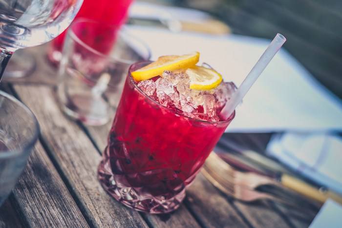 Red cocktail with ice and lemon slices on a wooden table
